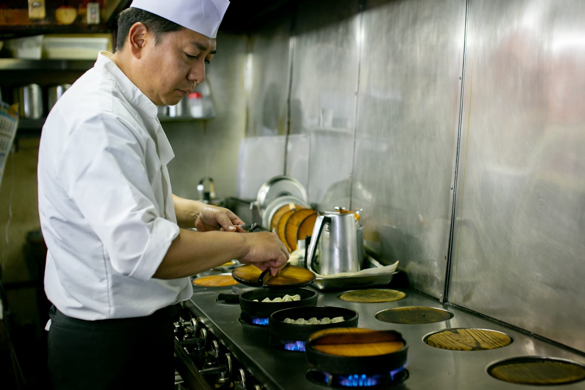 厨房で鉄なべに餃子を仕込む板長